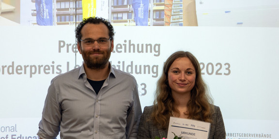 Julia Herbst und Dr. Schmalor nebeneinander auf der Preisverleihung, beide lächeln, Frau Herbst hält ihre Urkunde vor sich Julia Herbst und Dr. Schmalor nebeneinander auf der Preisverleihung, beide lächeln, Frau Herbst hält ihre Urkunde vor sich