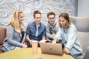 A group of four people looking on the screen of a laptop